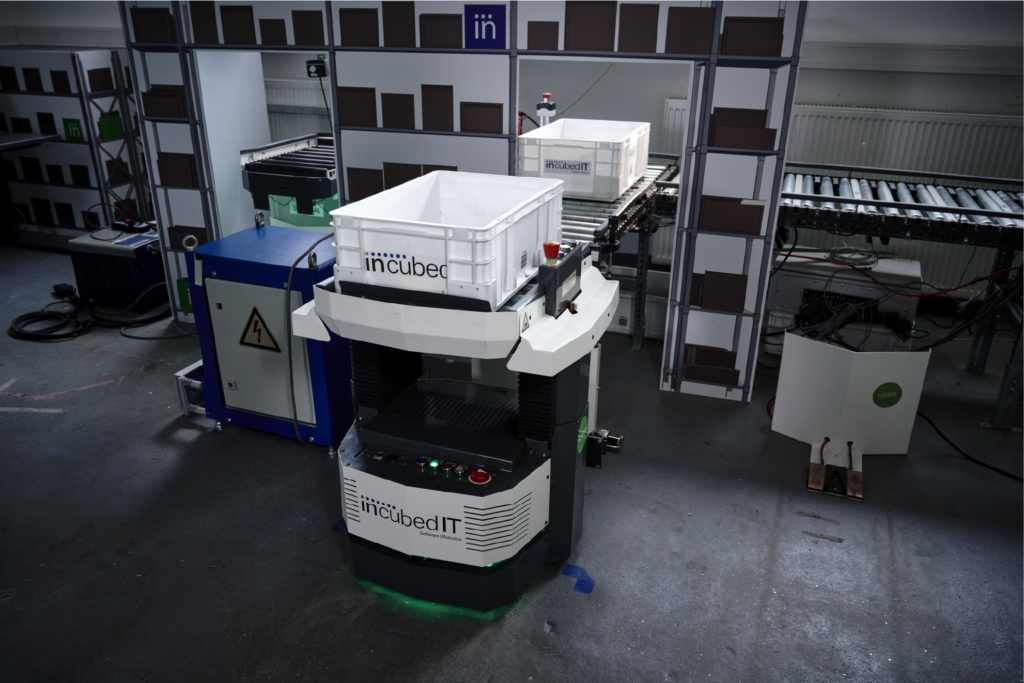 An AMR picking up a box from a rolling conveyor